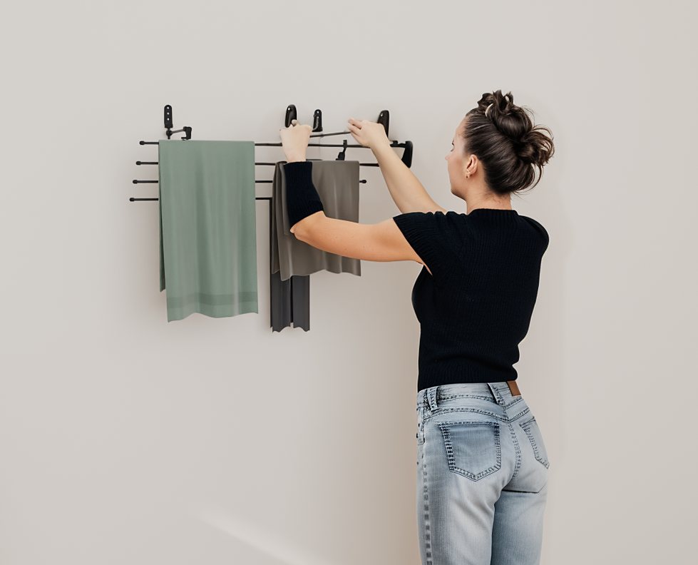A woman hangs a towel on the top rail of a black Airstair rack in a bright laundry room